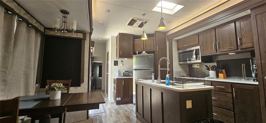 This kitchen and dining area features dark wood cabinetry, a center island, and stainless appliances — 3000 CLARCONA ROAD UNIT 2710, APOPKA, FL