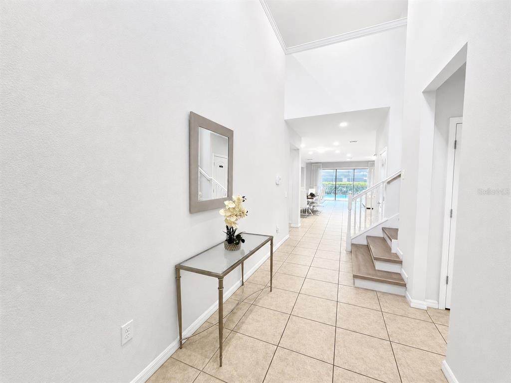 A bright entryway features tile flooring, a console table with a mirror, and a staircase — 8887 MENTON LOOP, KISSIMMEE, FL