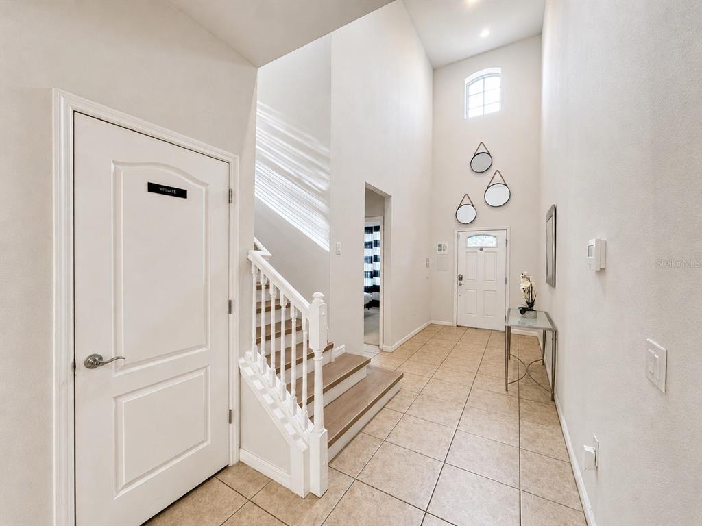 A bright entryway features tile flooring, a staircase with white railings, and a high ceiling — 8887 MENTON LOOP, KISSIMMEE, FL