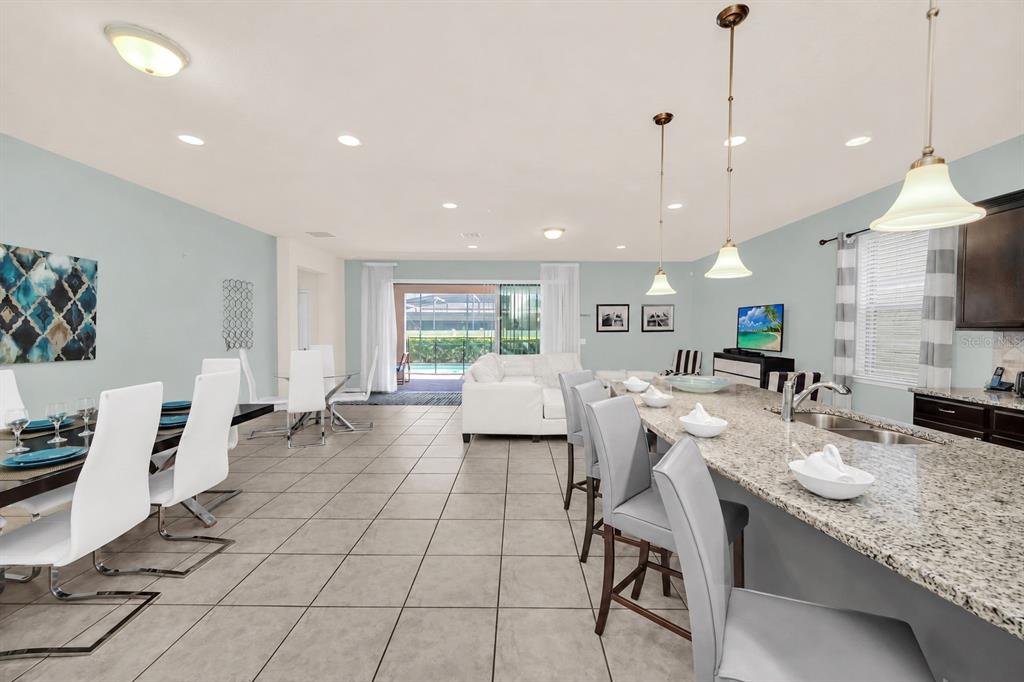 An open-concept kitchen and dining area features granite countertops, tile flooring, and a pool view — 8887 MENTON LOOP, KISSIMMEE, FL