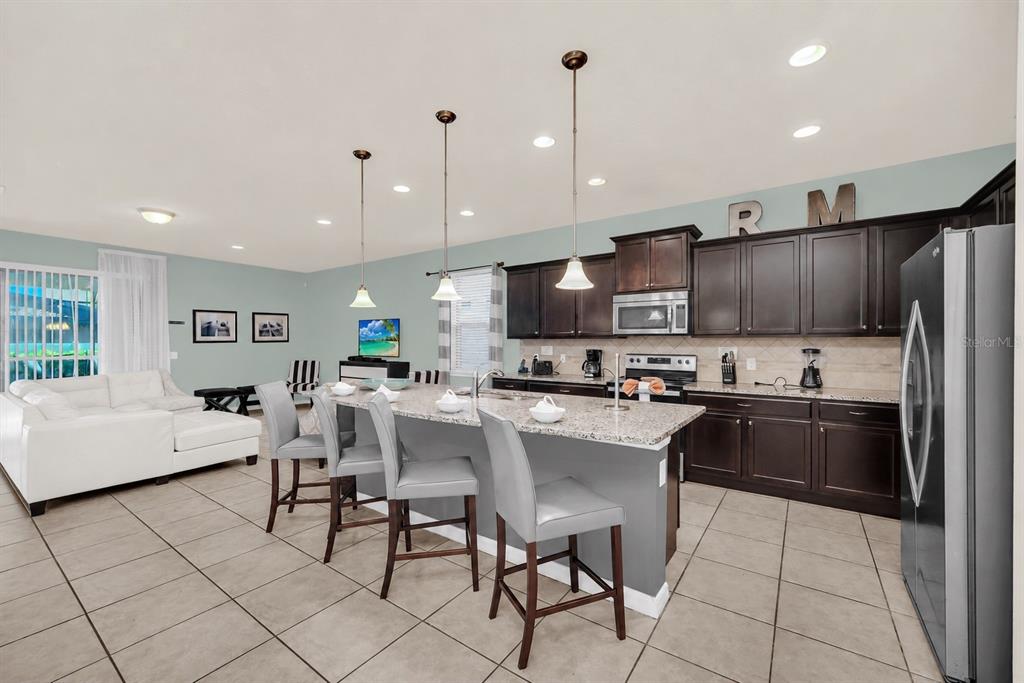 A kitchen with dark cabinets, granite countertops, and a breakfast bar with four gray stools — 8887 MENTON LOOP, KISSIMMEE, FL