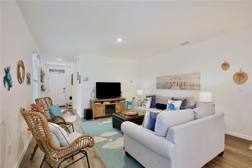 A living room features a light-colored sofa, two wicker chairs, a television, and coastal decor — 5356 HAYLOFT DRIVE, APOPKA, FL