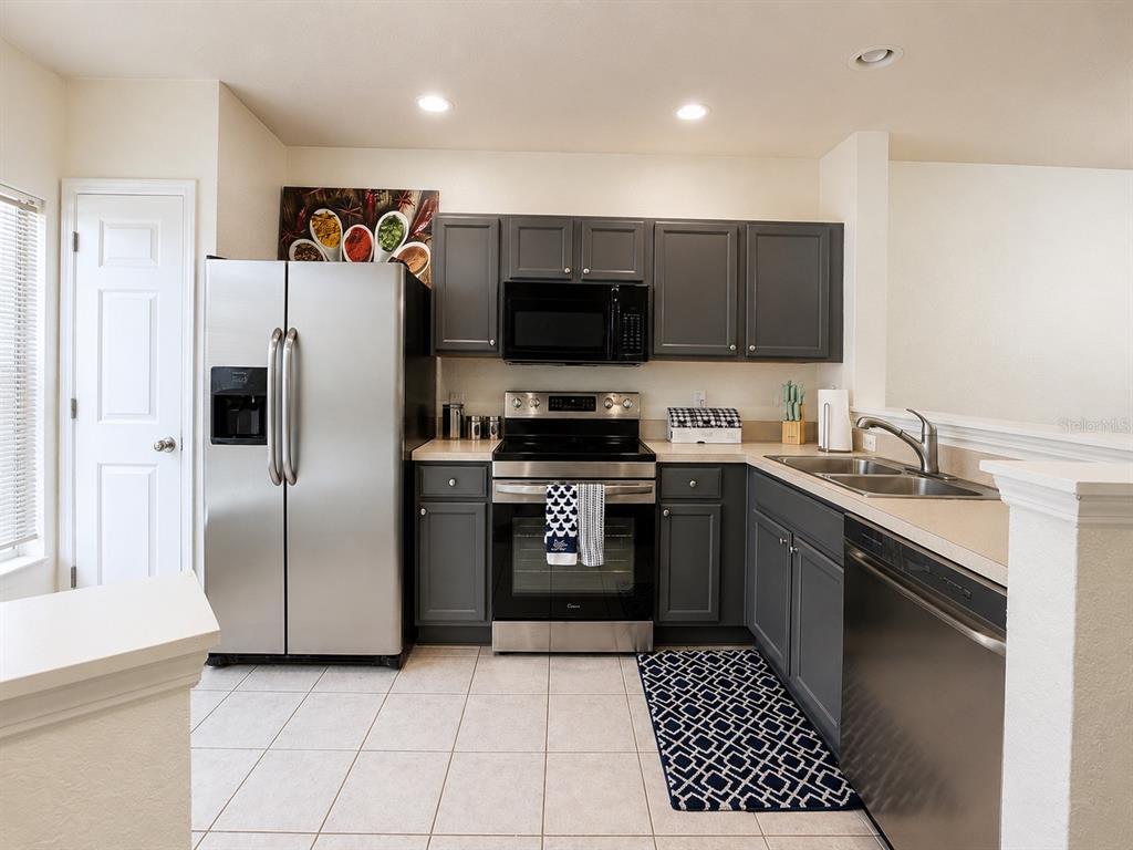 A kitchen features dark gray cabinets, stainless steel appliances, and light-colored tile flooring — 4452 SW 49TH AVENUE, OCALA, FL