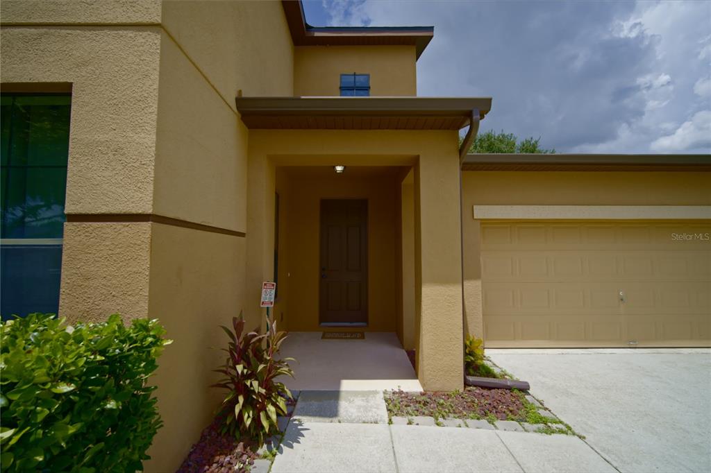 The exterior of a tan house features a covered entryway, a brown door, and a garage — 3087 POINTE PLACE AVENUE, KISSIMMEE, FL