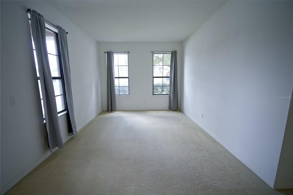 An empty room with beige carpet, white walls, and three windows with gray curtains — 3087 POINTE PLACE AVENUE, KISSIMMEE, FL
