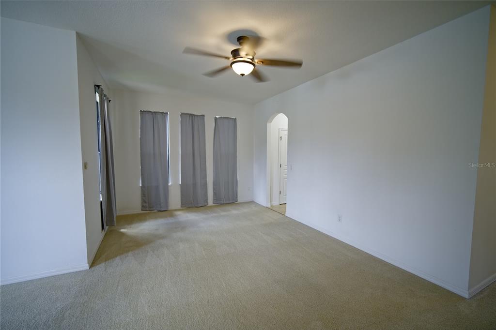An empty room with beige carpeting, white walls, a ceiling fan, and three windows — 3087 POINTE PLACE AVENUE, KISSIMMEE, FL