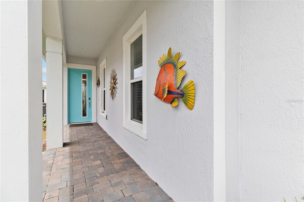 A covered porch features a teal front door, paver flooring, and decorative wall-mounted fish art — 2557 YELLOW BRICK ROAD, ST CLOUD, FL