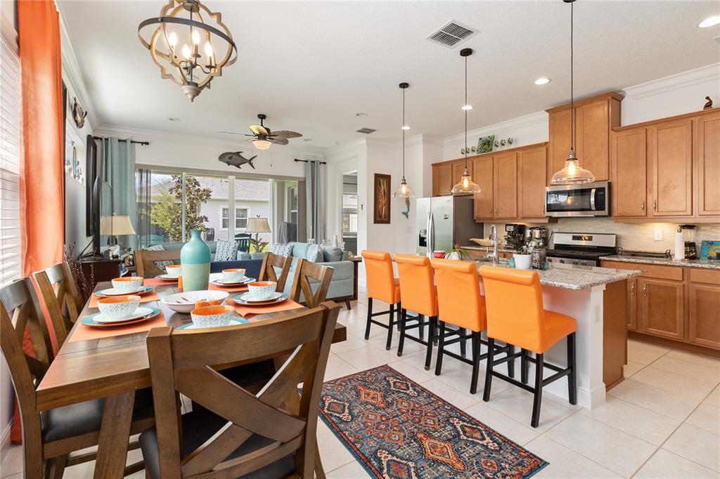 An open-concept kitchen and dining area features wooden cabinets, orange bar stools, and tile flooring — 2557 YELLOW BRICK ROAD, ST CLOUD, FL