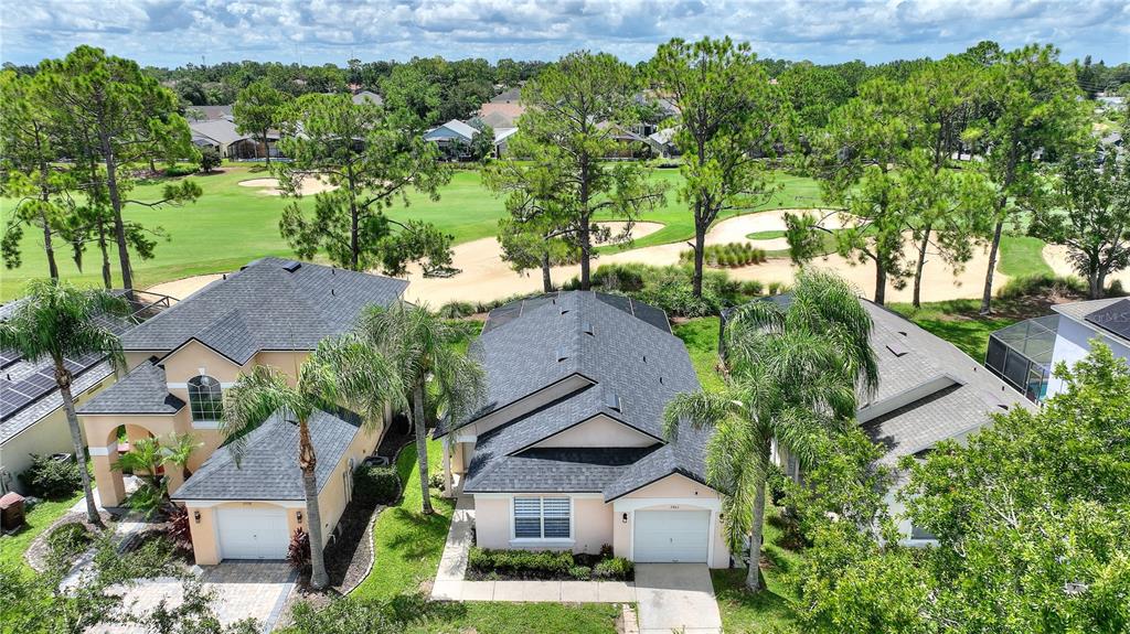 An aerial view shows three suburban houses with dark roofs situated along a golf course — 2960 KOKOMO LOOP, HAINES CITY, FL