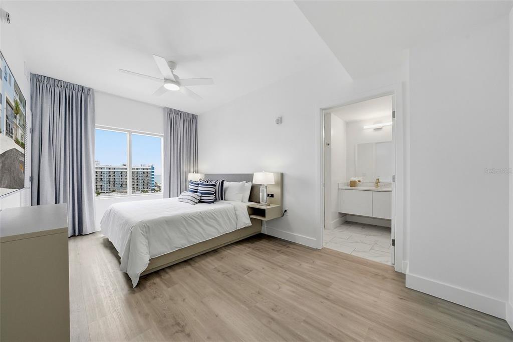 A modern bedroom features light wood flooring, a queen bed, and an attached bathroom — 411 E SHORE DRIVE UNIT 207, CLEARWATER BEACH, FL