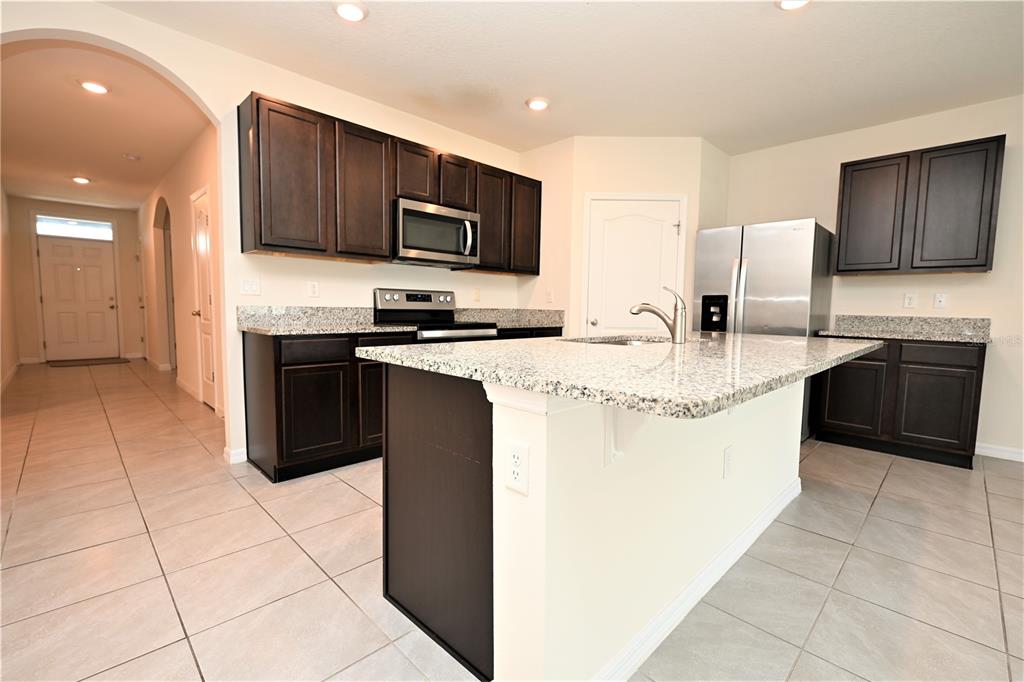 A kitchen features dark wood cabinets, granite countertops, a center island, and stainless steel appliances — 2548 RYLAND FALLS DRIVE, LAKELAND, FL