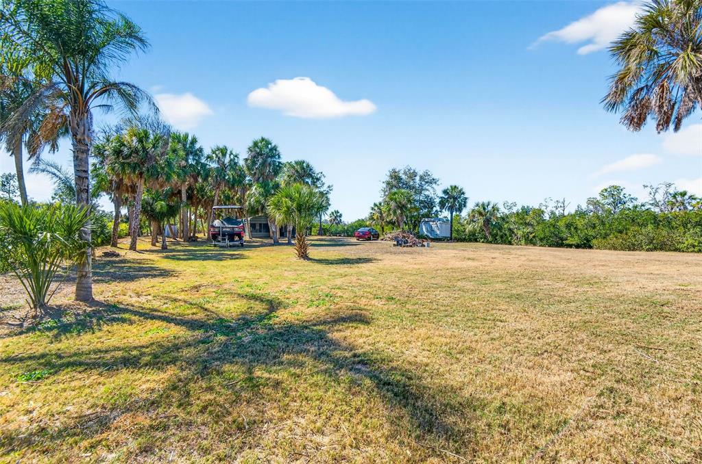 A large, grassy lot features several palm trees, a parked boat, and a red car — 2619 RIVER BEND DRIVE, RUSKIN, FL