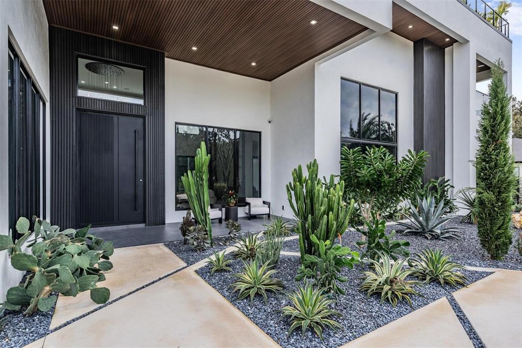 A modern home exterior features a dark front door, wood-paneled ceiling, and a desert-landscaped garden — 309 GRANDE GROVE COURT, LUTZ, FL