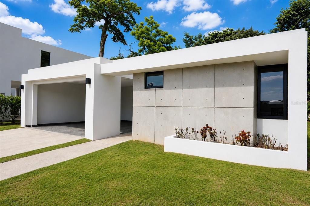 A modern house exterior features a concrete facade, a covered carport, and a white planter box — Apatita MONTEAZUL, GUAYNABO, PR