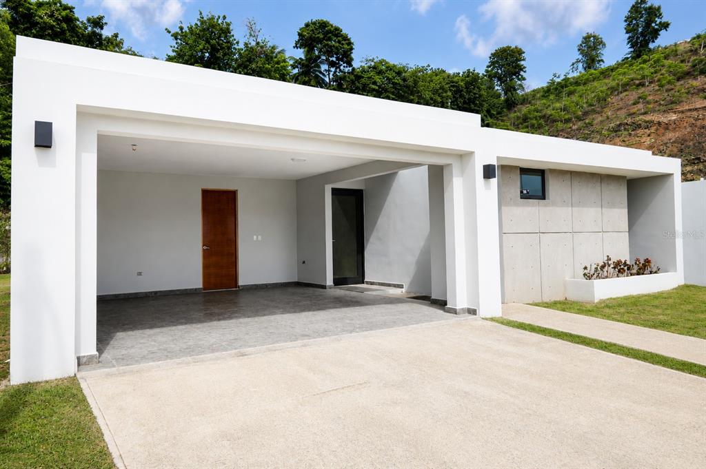 A modern white house exterior features a covered carport, a wooden door, and concrete panels — Apatita MONTEAZUL, GUAYNABO, PR