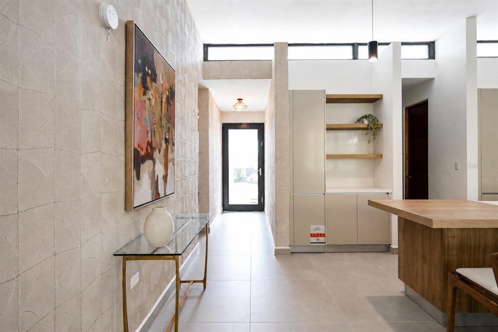 A modern entryway features a glass console table, textured wallpaper, and a view toward an exterior door — Apatita MONTEAZUL, GUAYNABO, PR