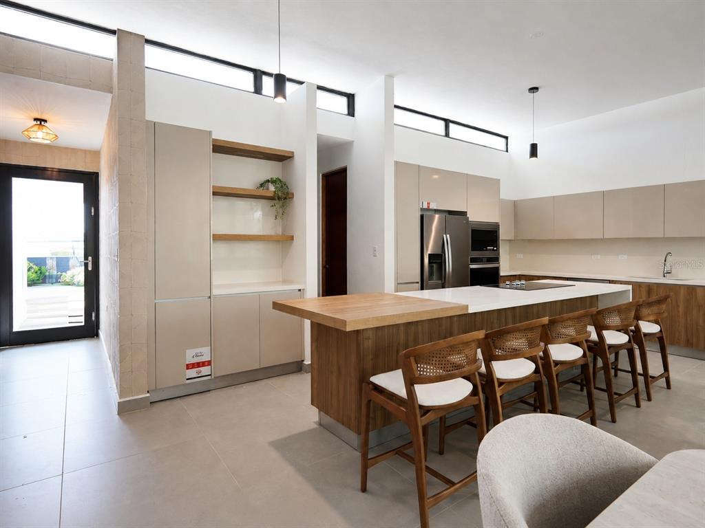 A modern kitchen features a wooden island with bar stools, light cabinetry, and clerestory windows — Apatita MONTEAZUL, GUAYNABO, PR