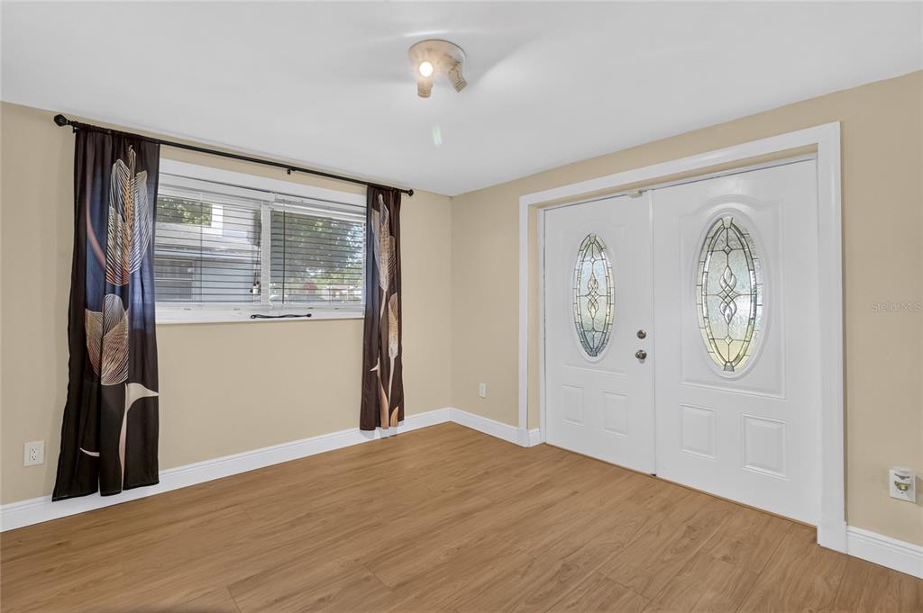A room with light wood-look flooring, beige walls, a window with curtains, and double doors — 3104 STEWART STREET, LAKELAND, FL