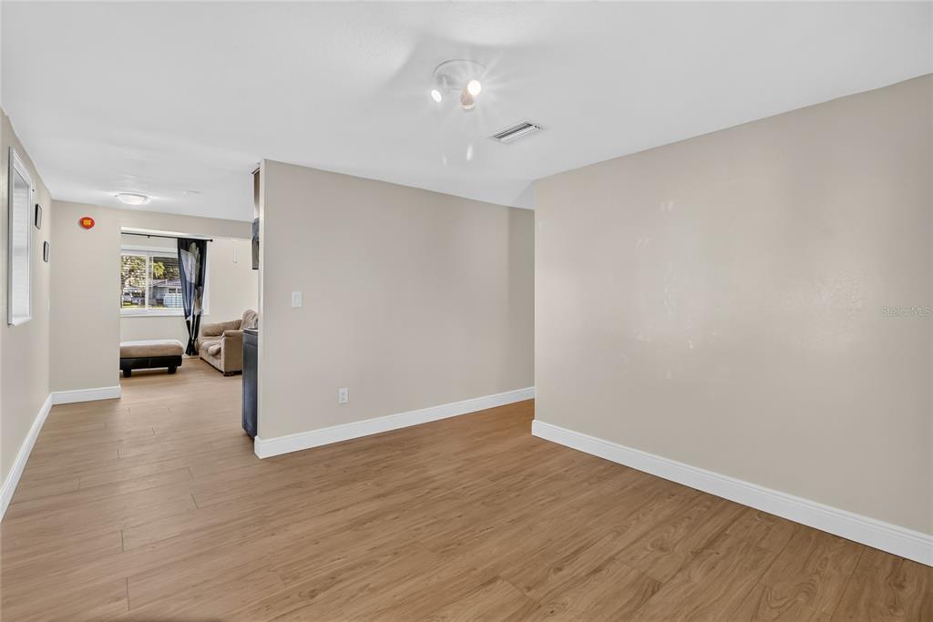An empty room with light wood-look flooring and beige walls leads to an adjacent living area — 3104 STEWART STREET, LAKELAND, FL