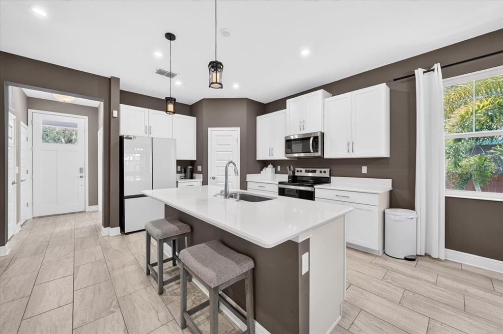 A modern kitchen features a white quartz island, white cabinetry, dark walls, and tile flooring — 1821 27TH STREET S, ST PETERSBURG, FL