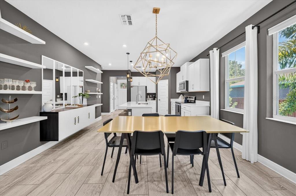 A dining area with a gold table and geometric chandelier opens into a modern kitchen — 1821 27TH STREET S, ST PETERSBURG, FL
