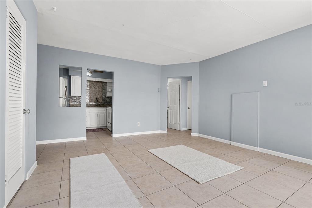 An empty room with light blue walls, tiled floors, and a pass-through to the kitchen — 522 FLORIDA AVENUE, CLEARWATER, FL