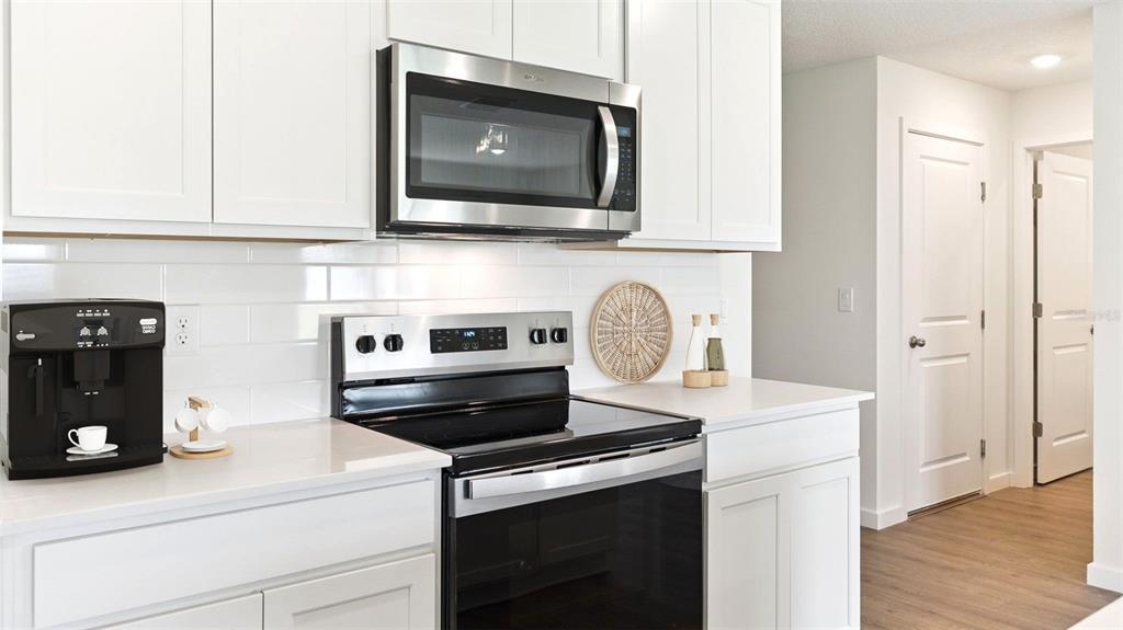A modern kitchen features white cabinetry, stainless steel appliances, and a white subway tile backsplash — 1484 MORNING WALK DRIVE, ORMOND BEACH, FL