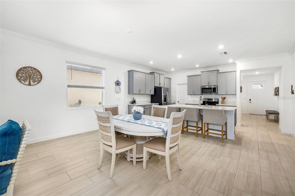 A bright, open-concept kitchen and dining area featuring gray cabinets, light tile floors, and island seating — 14281 17TH COURT E, PARRISH, FL