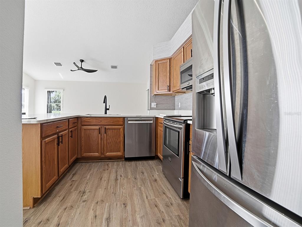 A kitchen features wood cabinets, stainless steel appliances, and wood-look flooring — 4438 RIVER RIDGE DRIVE, LEESBURG, FL