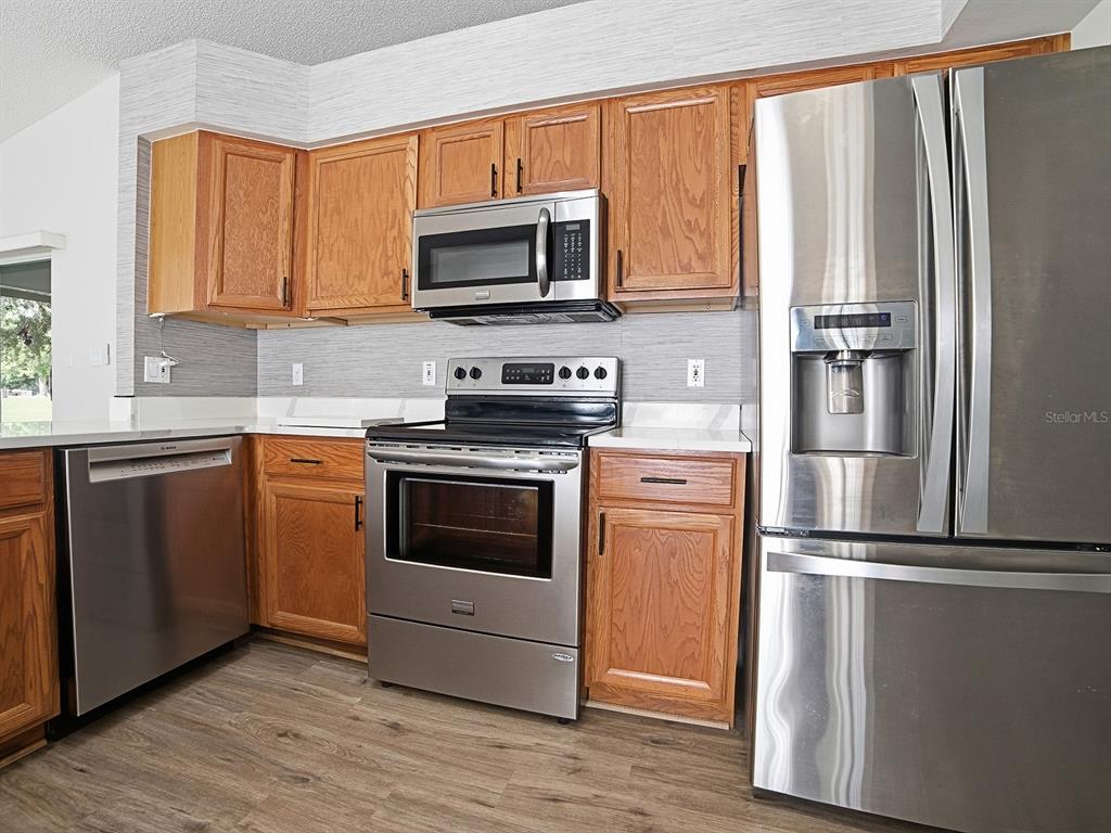 A kitchen features wood cabinets, stainless steel appliances, and light-colored countertops — 4438 RIVER RIDGE DRIVE, LEESBURG, FL