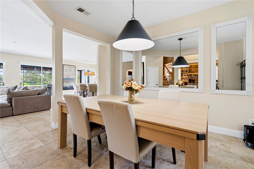 A dining room features a light wood table, upholstered chairs, a pendant light, and wall mirrors — 10355 EMERALD WOODS AVENUE, ORLANDO, FL