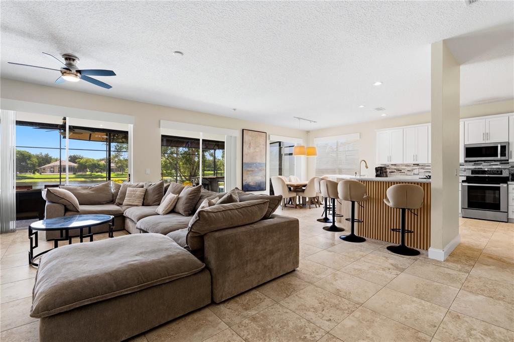 An open-concept living room and kitchen with tile flooring, a sectional sofa, and lake views — 10355 EMERALD WOODS AVENUE, ORLANDO, FL
