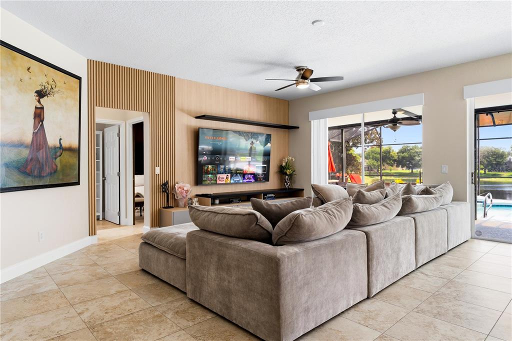 A living room features a large sectional sofa, a wood-slat accent wall, and sliding glass doors — 10355 EMERALD WOODS AVENUE, ORLANDO, FL