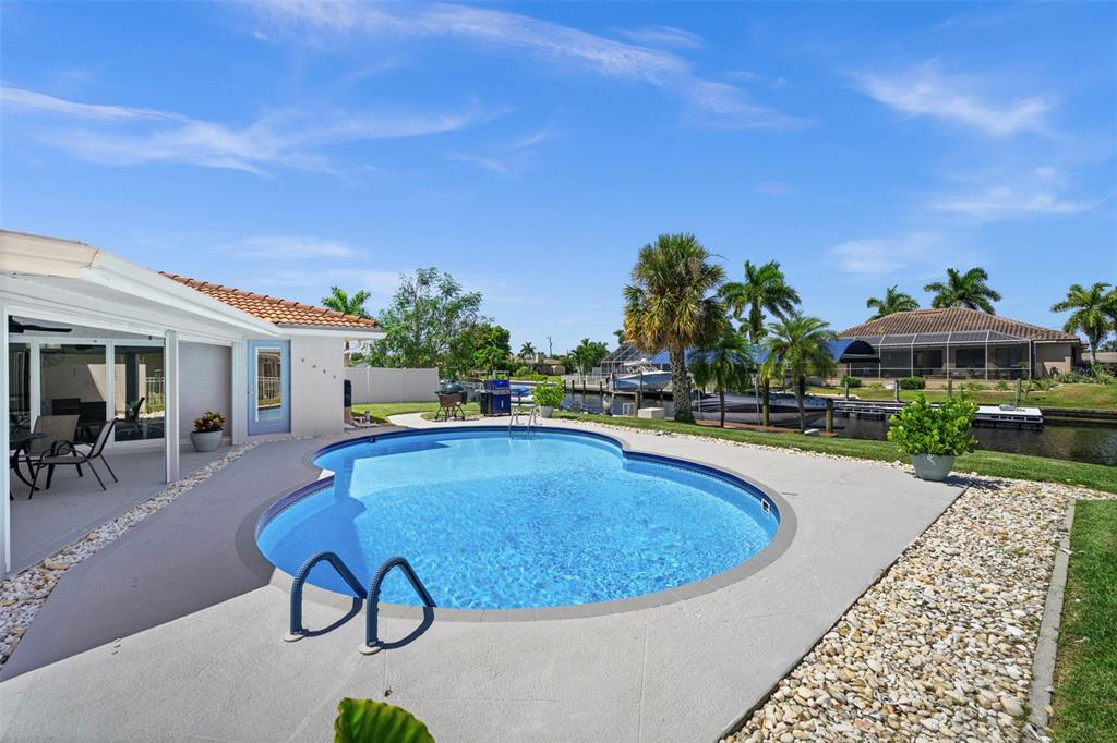 A backyard swimming pool sits on a concrete patio next to a canal with boats — 4914 SORRENTO COURT, CAPE CORAL, FL