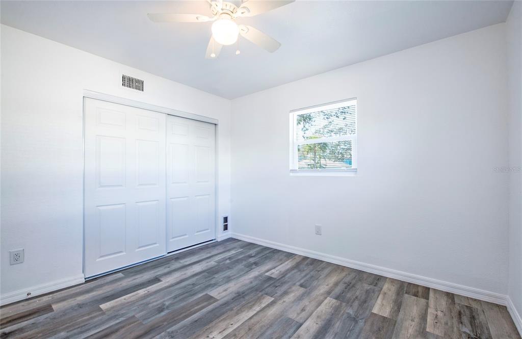 A bedroom features white walls, a ceiling fan, sliding closet doors, and wood-look flooring — 717 E GULF BOULEVARD UNIT 2, INDIAN ROCKS BEACH, FL