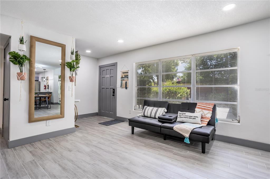 A living room features light wood-look tile floors, a black futon, and a large mirror — 1213 CORBETT LANE, ORLANDO, FL