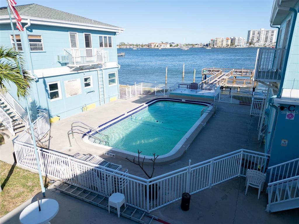 An elevated view of a swimming pool situated between two blue buildings overlooking the water — 483 E SHORE DRIVE UNIT D3, CLEARWATER BEACH, FL