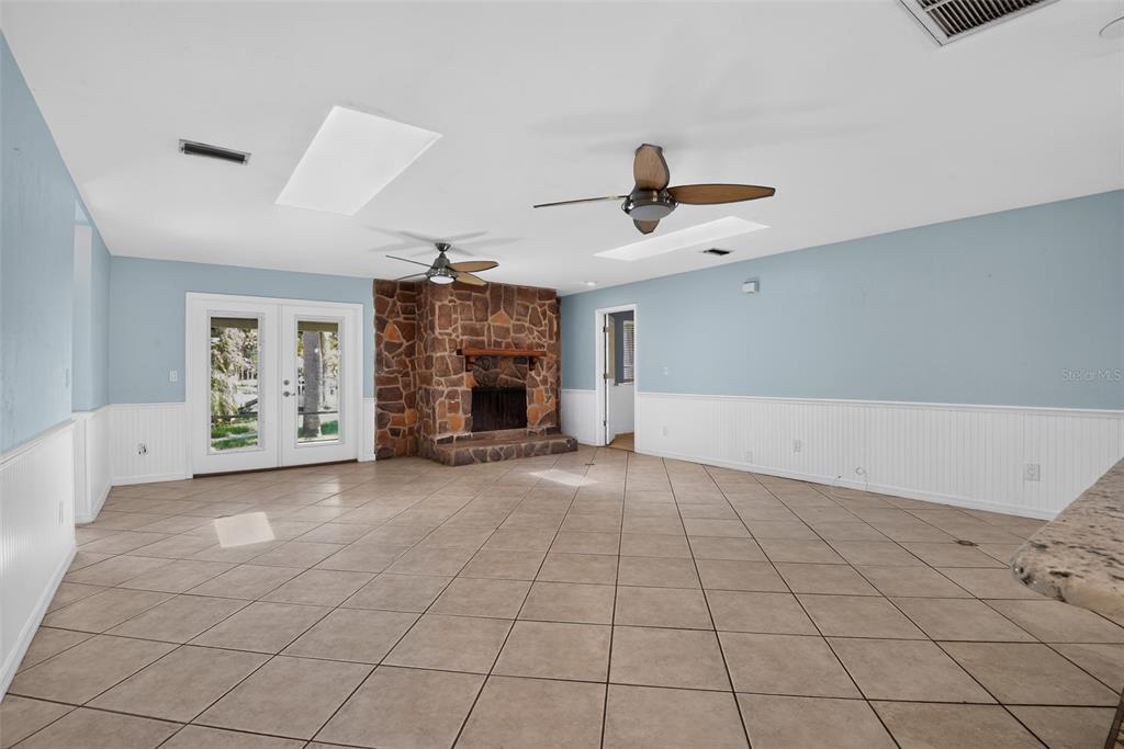 A spacious living room features light blue walls, white wainscoting, tile flooring, and a stone fireplace — 408 PALM AVENUE, ORMOND BEACH, FL