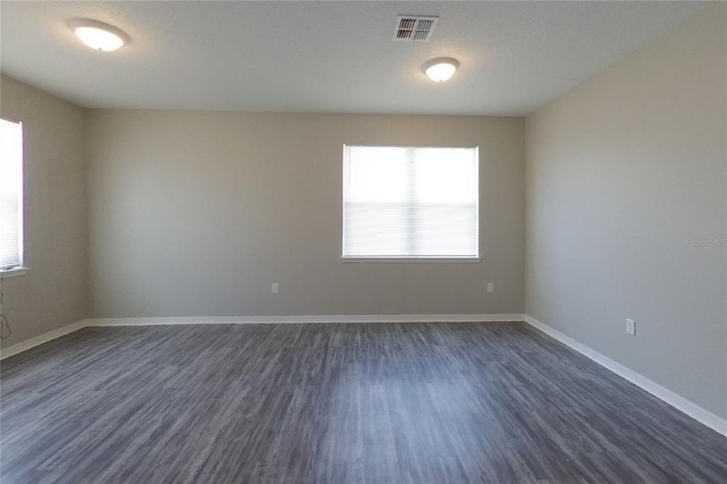 An empty room features light gray walls, wood-look flooring, two ceiling lights, and two windows — 226 BLACKSTONE CREEK ROAD, GROVELAND, FL