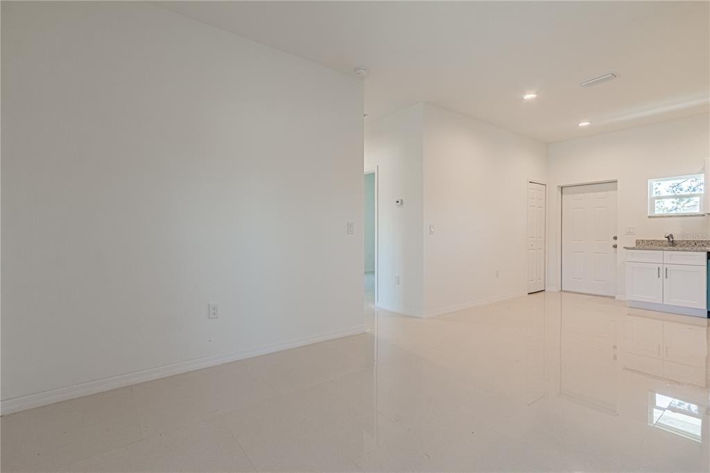 An open-concept room features white walls, light-colored tile flooring, and a small kitchen area — 753 PACIFIC STREET, LAKE PLACID, FL