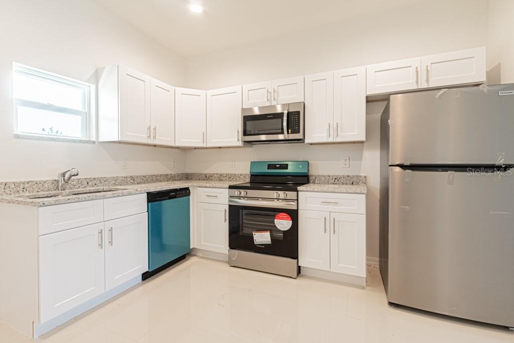A kitchen features white cabinets, granite countertops, stainless steel appliances, and a blue dishwasher — 753 PACIFIC STREET, LAKE PLACID, FL