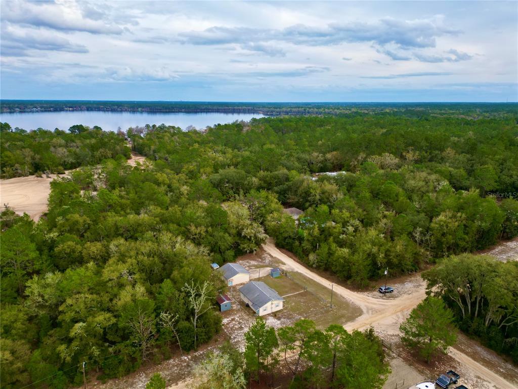 An aerial view shows a house and outbuilding surrounded by trees near a large lake — 600 WAKULLA STREET, FLORAHOME, FL