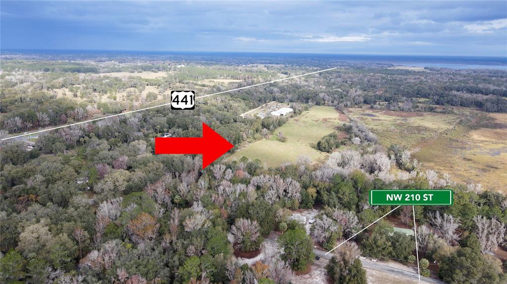 An aerial view shows a large, grassy field surrounded by trees near a highway — 5725 NW 210TH STREET, MICANOPY, FL