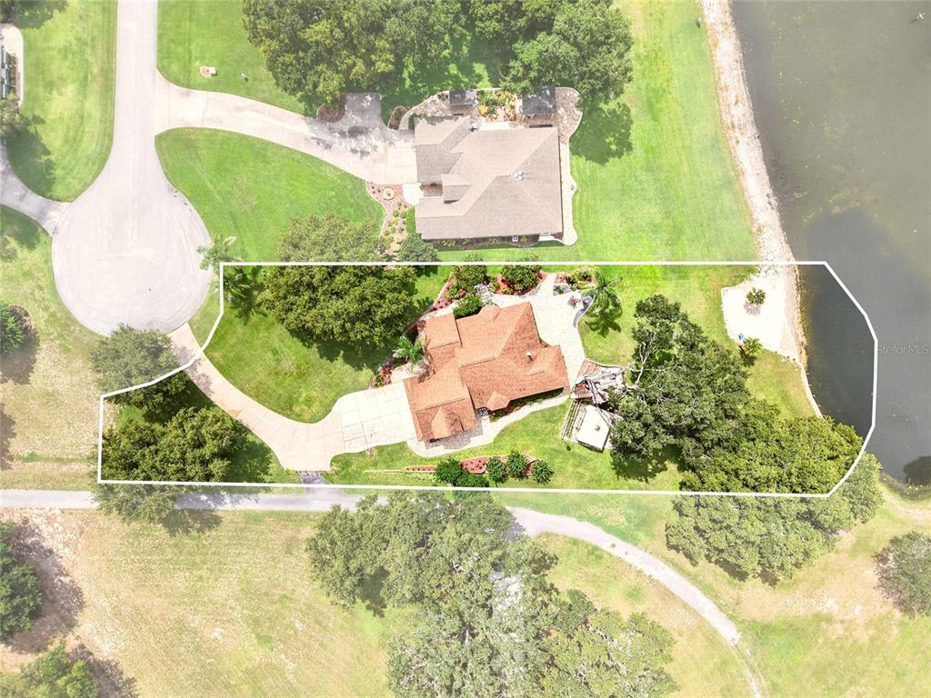 An aerial view shows a house with a brown roof, driveway, and yard beside water — 1833 SHORE LINE DRIVE, LEESBURG, FL