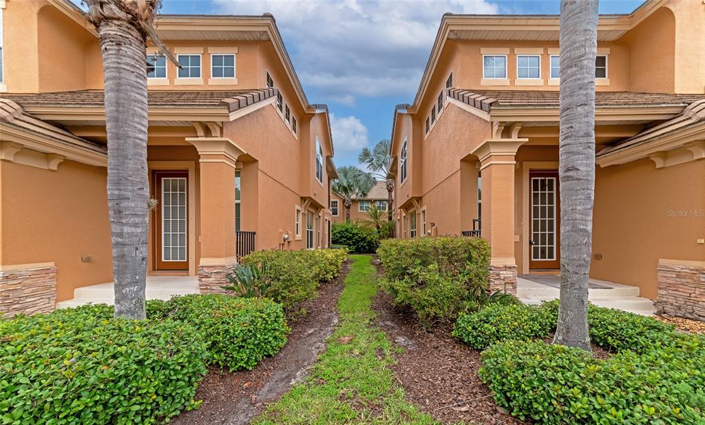 Two tan townhomes with palm trees and landscaping in front under a cloudy sky — 5519 NAPA DRIVE, SARASOTA, FL