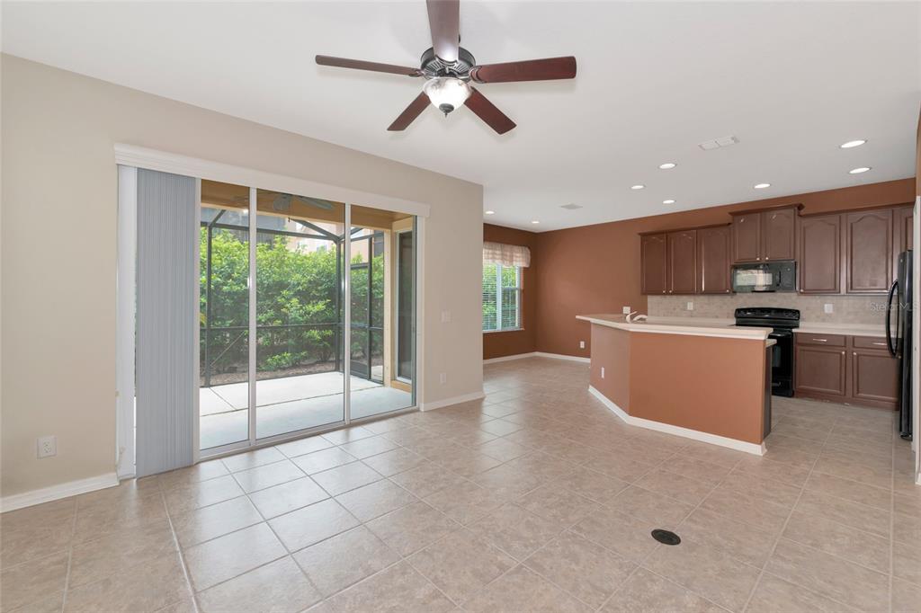 An open-concept kitchen and dining area with tile flooring, brown cabinets, and sliding glass doors — 5519 NAPA DRIVE, SARASOTA, FL
