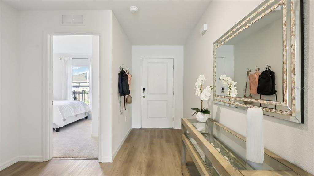 A bright entryway features wood-look flooring, a console table with a mirror, and a doorway — 15014 CROSSHALL STREAM DRIVE, WIMAUMA, FL