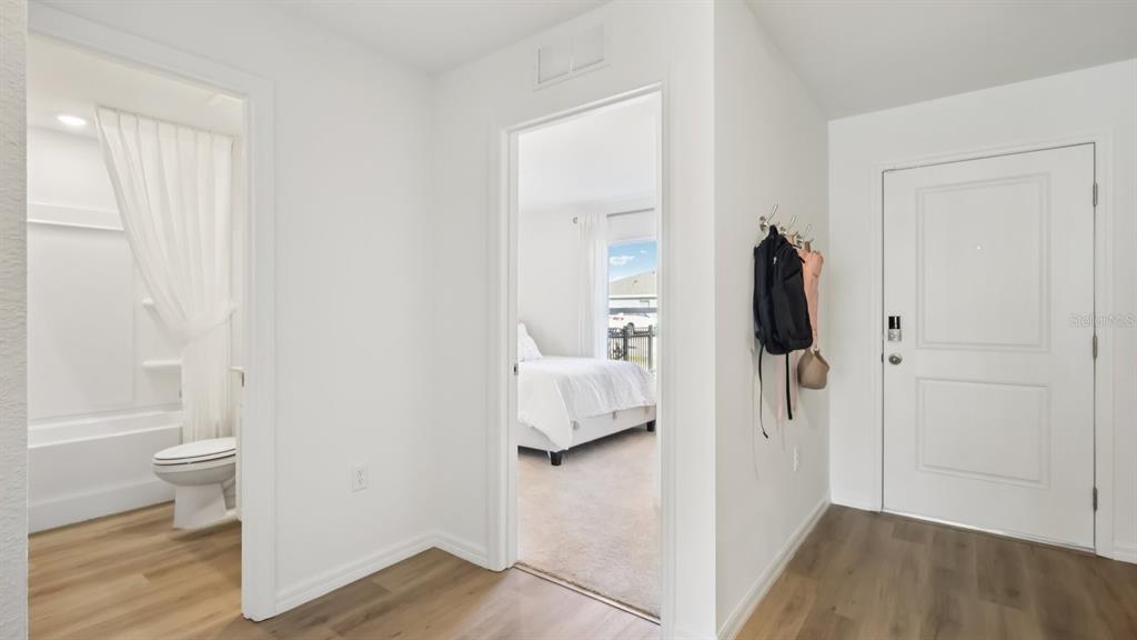 A hallway with wood-look flooring leads to a bathroom and a bedroom with white bedding — 15014 CROSSHALL STREAM DRIVE, WIMAUMA, FL