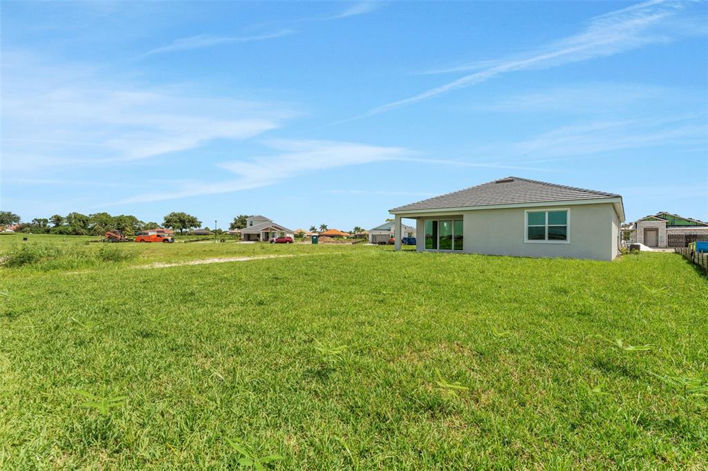 A view of the grassy backyard and rear exterior of a single-story suburban house — 16930 SQUIRREL BRANCH LANE, ALVA, FL