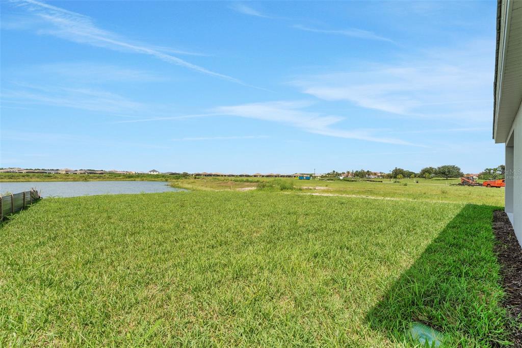 A grassy backyard overlooks a pond and a distant residential neighborhood under a blue sky — 16930 SQUIRREL BRANCH LANE, ALVA, FL